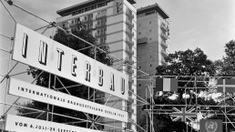 Tafeln an einem Baugerüst mit Schildern, auf denen steht: „Interbau – Internationale Bauausstellung Berlin 1957 – vom 6. Juli bis 29. September geöffnet von 9 bis 19 Uhr“