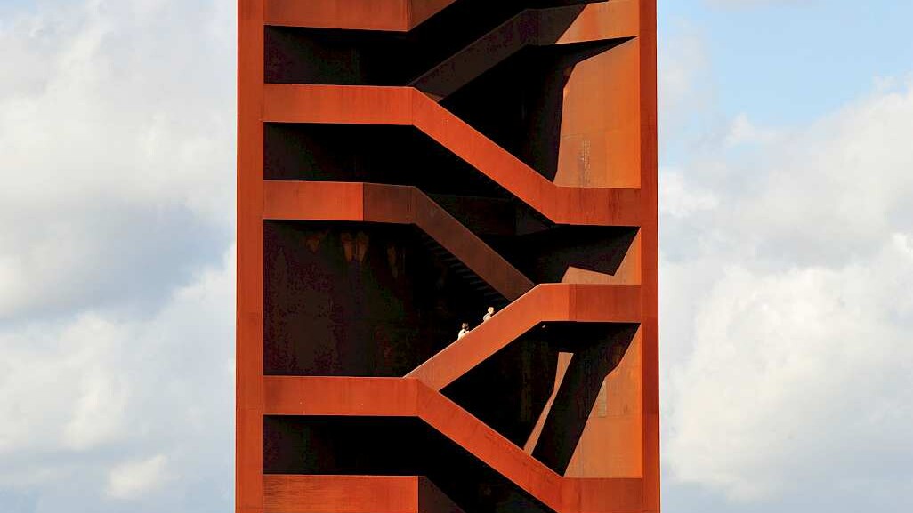 der skulpturale Turm mit Einblick in die offenen Treppenstrukturen im Inneren, oben stehen Menschen und blicken in die Landschaft