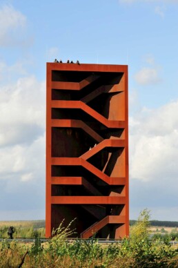 der skulpturale Turm mit Einblick in die offenen Treppenstrukturen im Inneren, oben stehen Menschen und blicken in die Landschaft