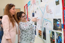 eine Schülerin präsentiert einer Frau ihre Abschlussarbeit an einer Stellwand mit Zeichnungen und Texten